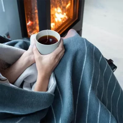 Sitting by a fireplace with a cup of tea wrapped in a blanket